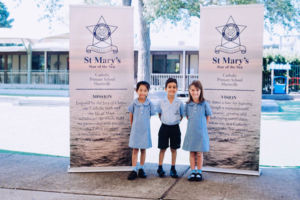 Three students standing in front of St Mary Star of the Sea Catholic Primary School Hurstville banners